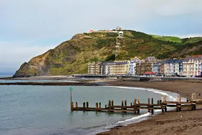 a beach with a pier and buildings on a hill at Parc y Bryn Serviced Apartments in Aberystwyth