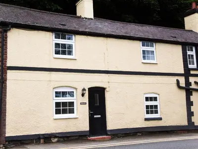 a yellow house with white windows and a black door at Minafon in Llangollen