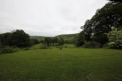 a large green field with trees and hills in the background at Plas Esgair in Llanbrynmair