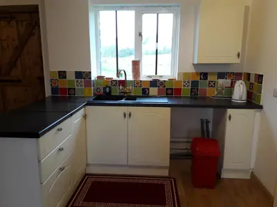 a kitchen with white cabinets and a sink and a window at The Barn Annexe, Cefn-Yr-Allt in Crickadarn