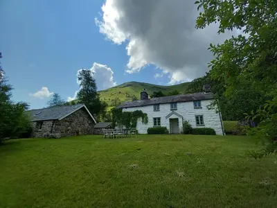 a white house with a hill in the background at Gesail Barn and Farmhouse in Machynlleth