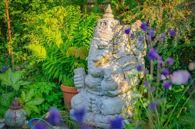 a stone statue in a garden with purple flowers at The Rose Barn, Ysgubor y Rhosyn in Llandysul
