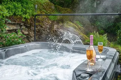 a hot tub with a bottle and two glasses of wine at Hawddamor in Dolgellau