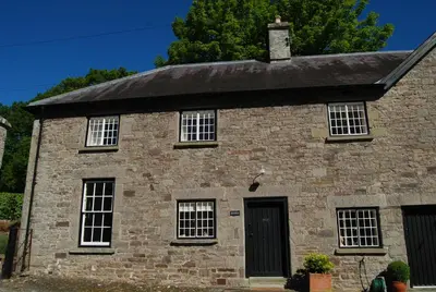an old stone house with white windows and a black door at Glanhenwye Courtyard Cottages in Glasbury