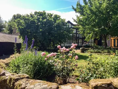 a garden in front of a house with pink roses at The Old Barn in Hereford