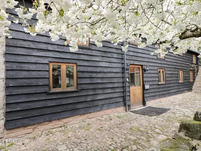 a house with black siding and a tree with white flowers at The Old Barn in Hereford
