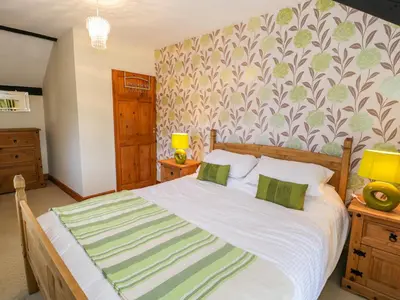 a bedroom with a large white bed with green pillows at The Stable Cottage in Llanbedr