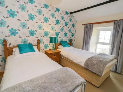 two beds in a bedroom with blue flowers on the wall at The Stable Cottage in Llanbedr