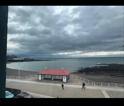 two people walking past a small building on the beach at Luxury Sea View Apartment - One Bedroom in Aberystwyth