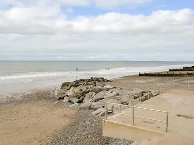 a sandy beach with a staircase leading to the ocean at Gwynt Y Môr in Tywyn