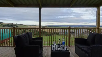 a porch with two chairs and a table with wine glasses at Woodbatch Camping & Glamping in Bishops Castle