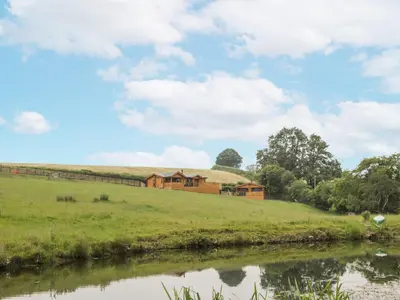 a house on a hill next to a river at Manor Farm Lodges - Red Kite Lodge in Newtown