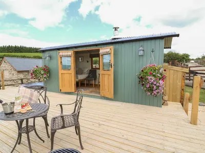 a green shed with a table and chairs on a deck at Ivy's Way in Rhayader