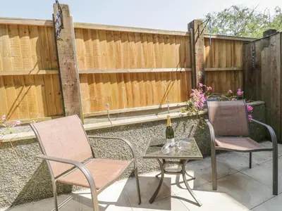 a patio with two chairs and a table with a bottle of wine at Angorfa in Llanbedr