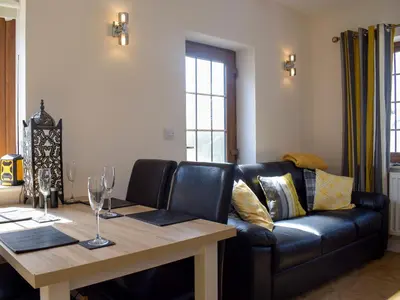 a living room with a black leather couch and a wooden table at Windhover in Glasbury