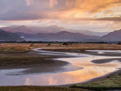 a river in a field with mountains in the background at Moelwyn View Cottage in Blaenau-Ffestiniog