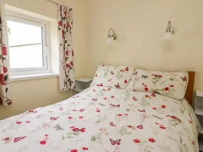 a bed with a floral comforter and a window at Hen Brynbedw in Llanybydder