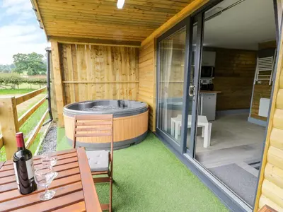 a deck with a hot tub and a table with a bottle of wine at Cilan Lodge in Corwen