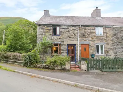 a stone house with an orange door on a street at Dyfi Cottage in Machynlleth