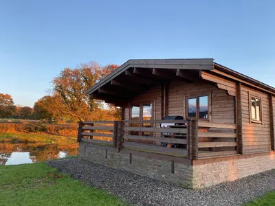 a log cabin with a deck next to a pond at RedWood Lodge in Ludlow