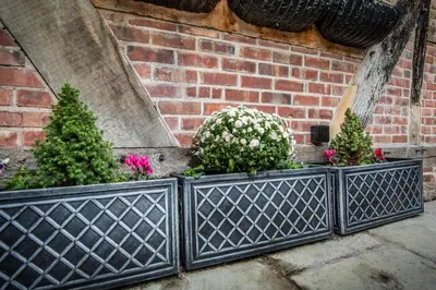 a black fence with flowers and plants in front of a brick wall at 