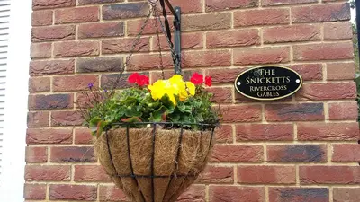a flower basket hanging on a brick wall with a sign at The Snicketts in Ludlow