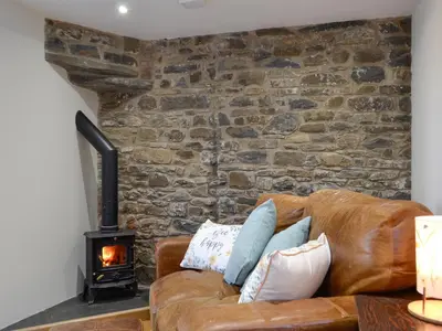 a living room with a leather couch and a wood stove at Cornel Clyd Cosy Corner in Cilcennin