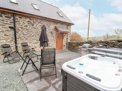 a hot tub and chairs on a patio with a building at Stabl, Plas Moelfre Hall Barns in Oswestry