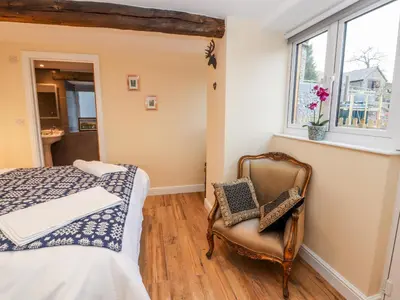 a bedroom with a bed and a chair and a window at Stabl, Plas Moelfre Hall Barns in Oswestry
