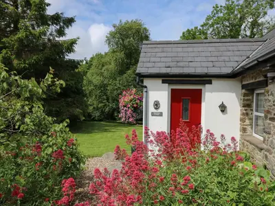a cottage with a red door in a garden with flowers at Trawsnant Cottage in New Quay