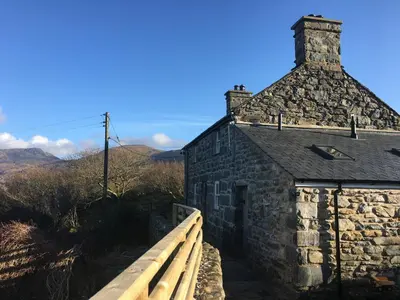 an old stone building with a wooden fence next to it at Gellibant Cottage in Llanbedr
