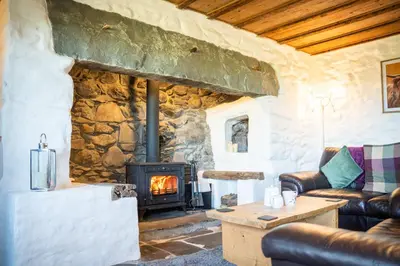 a living room with a wood stove in a stone wall at Gellibant Cottage in Llanbedr