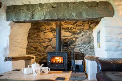 a stone fireplace in a living room with a wood stove at Gellibant Cottage in Llanbedr