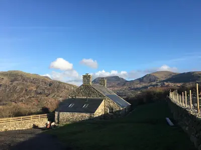 an old stone house with mountains in the background at Gellibant Cottage in Llanbedr