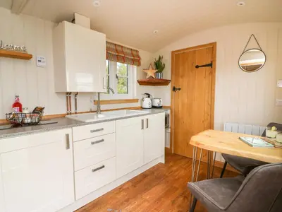a kitchen with white cabinets and a wooden table at Marches Way in Rhayader
