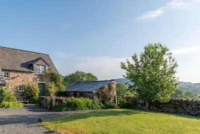 an old stone house with a stone wall and a yard at Alltybrain Farm Cottages in Brecon