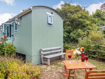 a green shed with a bench and a table with wine glasses at The Shepherd's Hut in Aberdyfi