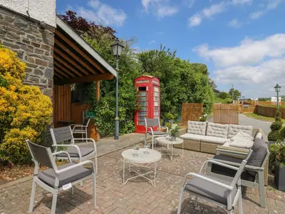 a patio with chairs and a red phone booth at Llety Ceiro in Bow Street