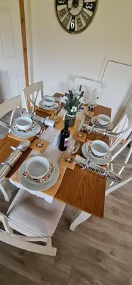 a dining table with plates and glasses and a clock at Bennar Isa Cottages Dyffryn Ardudwy in Barmouth