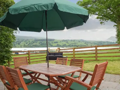 a wooden table with chairs and an umbrella at Bwthyn Glanllyn in Llanuwchllyn