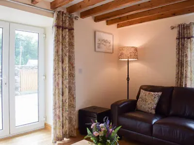 a living room with a leather couch and a window at Bwthyn Glanllyn in Llanuwchllyn