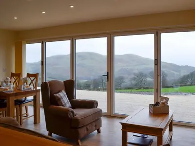 a living room with a chair and a table and windows at Sweet Meadow Lodge in Llandrindod Wells