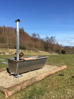 a woman sitting in a bath tub in a field at Belan Bluebell Woods Shepherds Hut in Llanidloes