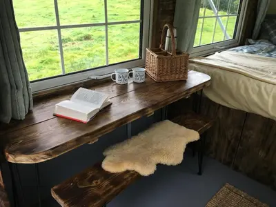 a table with two books and two mugs and a window at Belan Bluebell Woods Shepherds Hut in Llanidloes