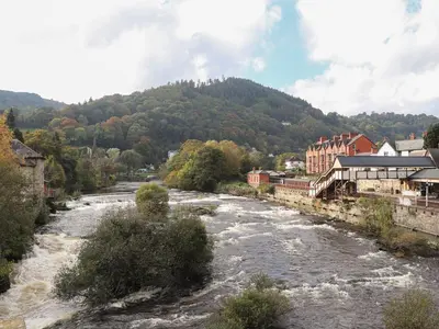 a river in a town next to a mountain at Whitewater Cottage in Llangollen