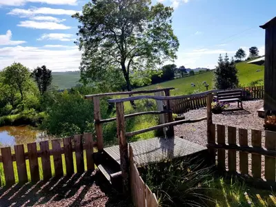 a wooden fence with a bench next to a river at Cornflour Cozy Cabin Retreat in Craven Arms