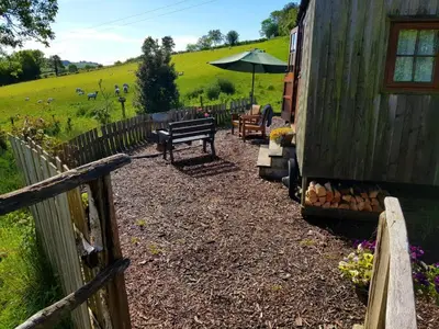 a garden with a bench and an umbrella next to a building at Cornflour Cozy Cabin Retreat in Craven Arms