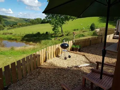 a barbecue grill in a yard next to a fence at Cozy Cabin Retreat - Sleeps 2 & a Child in Craven Arms