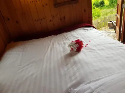 a white bed with a bouquet of flowers on it at Cozy Cabin Retreat - Sleeps 2 & a Child in Craven Arms