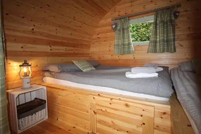a bed in a log cabin with a window at Torrent Walk Glamping Huts in the Heart of Snowdonia in Dolgellau